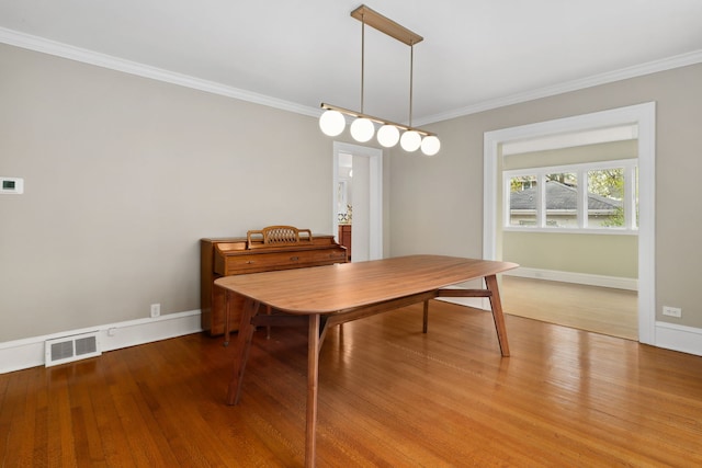 dining space featuring baseboards, crown molding, wood finished floors, and visible vents