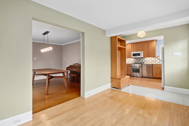 kitchen featuring tasteful backsplash, light wood-type flooring, stainless steel appliances, decorative light fixtures, and baseboards