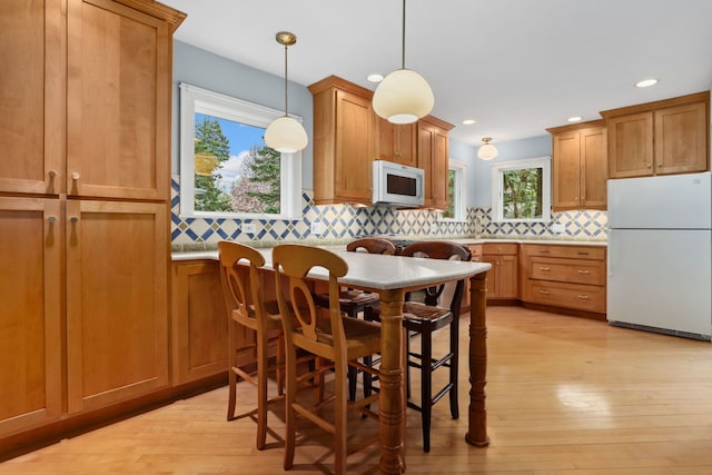 kitchen featuring brown cabinetry, backsplash, white appliances, and plenty of natural light