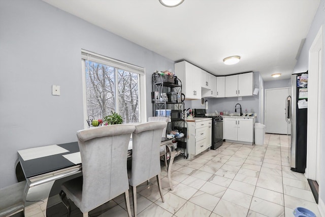 kitchen with white cabinets, a sink, freestanding refrigerator, black gas range oven, and light countertops