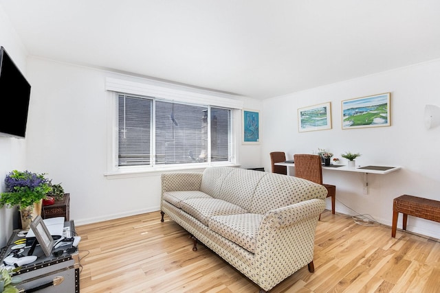 living area with ornamental molding, baseboards, and light wood-type flooring