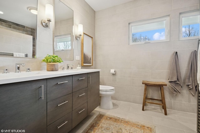 bathroom with double vanity, toilet, tile walls, plenty of natural light, and tile patterned flooring