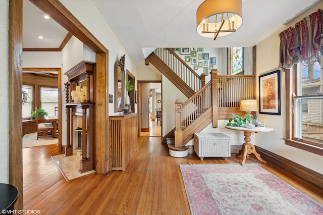 entryway with wood finished floors, stairway, and crown molding