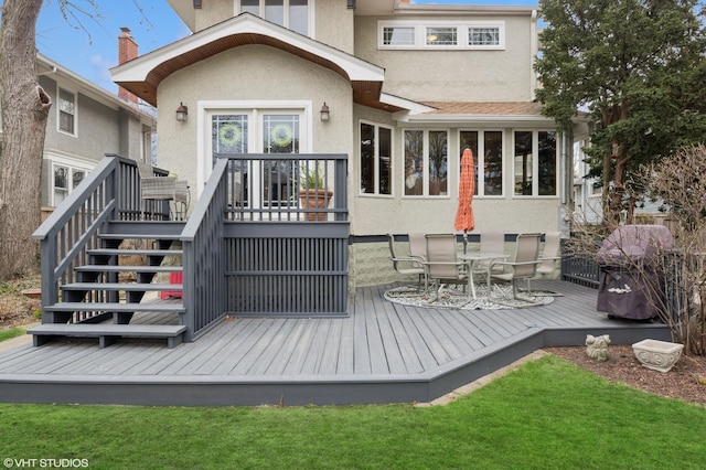 rear view of house with stucco siding, a wooden deck, stairway, and outdoor dining space