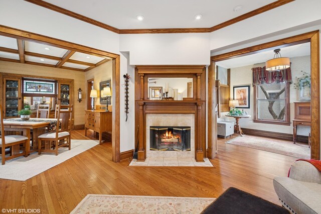 living area featuring baseboards, a tiled fireplace, wood finished floors, and ornamental molding