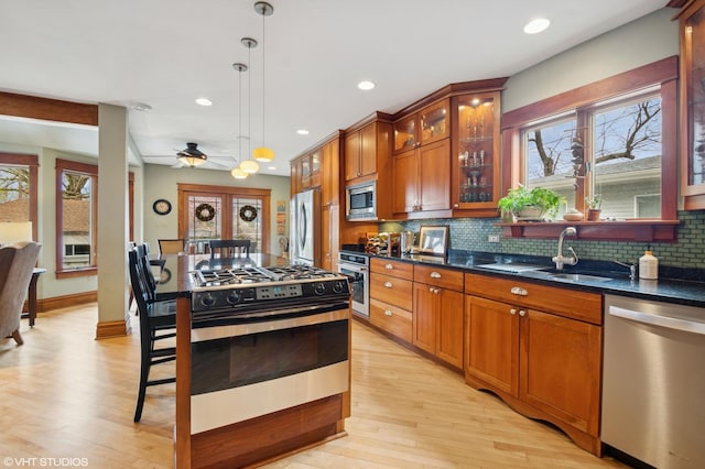 kitchen featuring light wood finished floors, pendant lighting, brown cabinets, and appliances with stainless steel finishes
