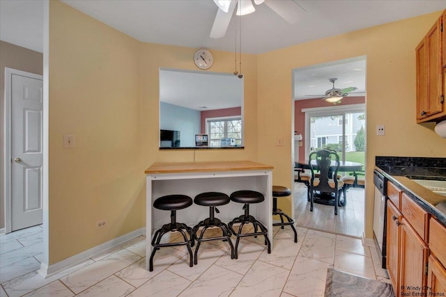 kitchen with brown cabinetry, marble finish floor, baseboards, a ceiling fan, and dishwasher