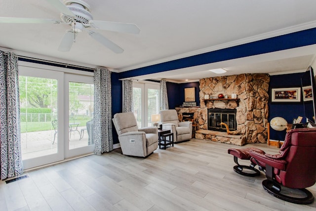 living area featuring a ceiling fan, a stone fireplace, visible vents, crown molding, and wood finished floors