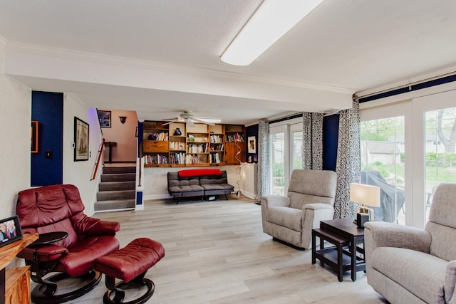 living area with a ceiling fan, stairway, baseboards, light wood-style floors, and ornamental molding