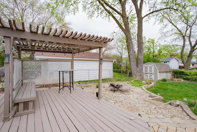 wooden terrace with an outdoor fire pit, a storage shed, a fenced backyard, a lawn, and an outdoor structure