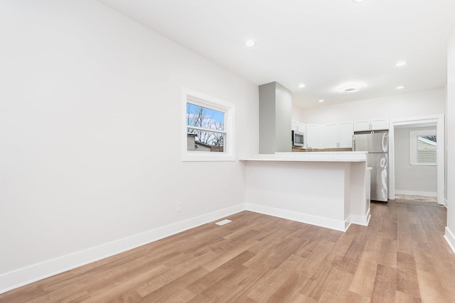 kitchen featuring light countertops, light wood finished floors, baseboards, a peninsula, and appliances with stainless steel finishes