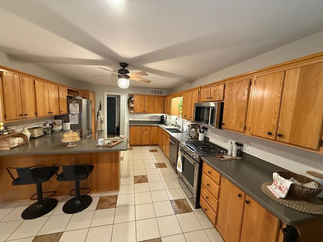 kitchen with dark countertops, appliances with stainless steel finishes, a sink, a peninsula, and visible vents