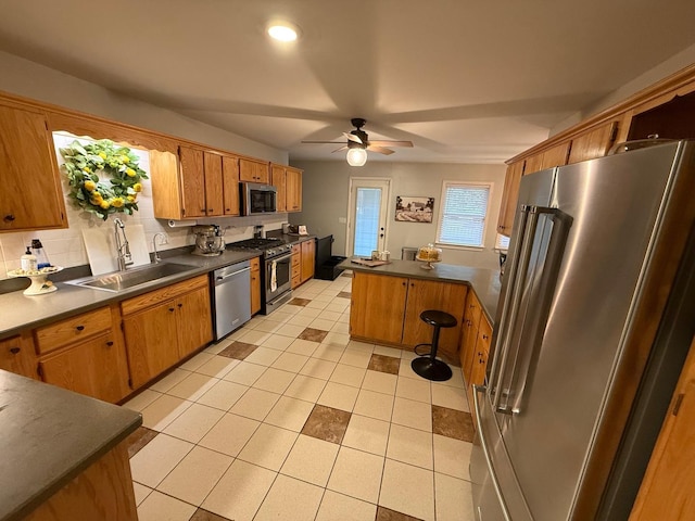 kitchen featuring stainless steel appliances, dark countertops, a sink, and a peninsula