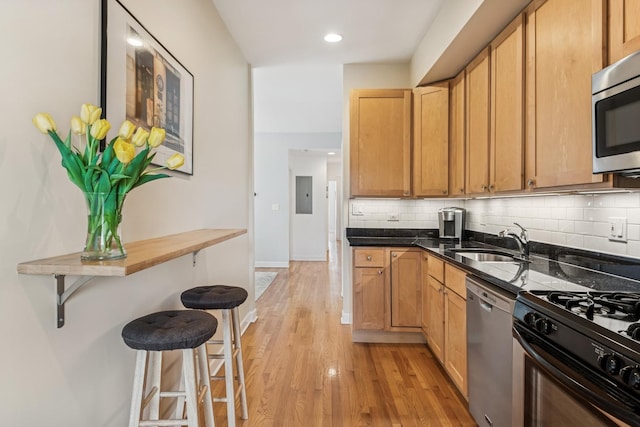 kitchen featuring appliances with stainless steel finishes, tasteful backsplash, a sink, light wood-type flooring, and a kitchen bar
