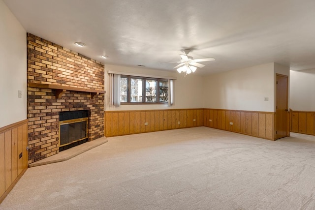 unfurnished living room with wainscoting, ceiling fan, carpet floors, and wood walls