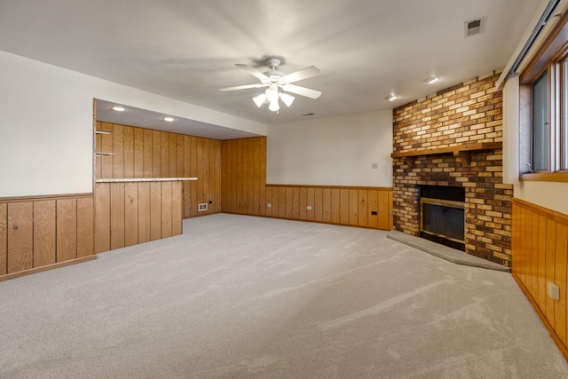 unfurnished living room featuring a wainscoted wall, visible vents, light colored carpet, a ceiling fan, and wood walls