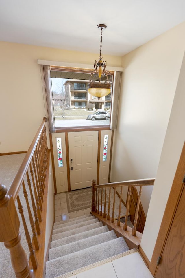 tiled entryway featuring stairs, a chandelier, and baseboards