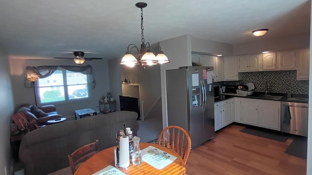 kitchen featuring white cabinets, dark countertops, a sink, light wood-style flooring, and appliances with stainless steel finishes