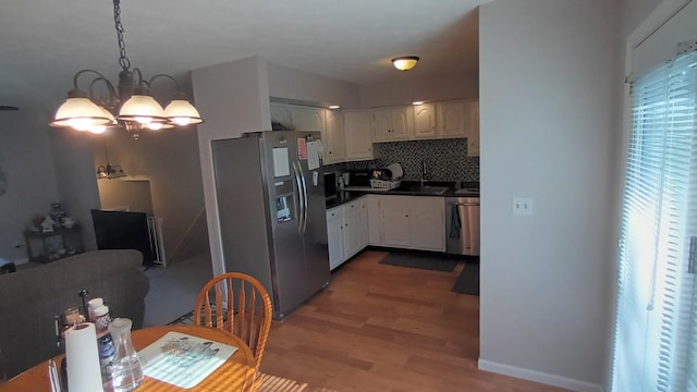kitchen featuring stainless steel appliances, light wood-type flooring, dark countertops, an inviting chandelier, and white cabinetry
