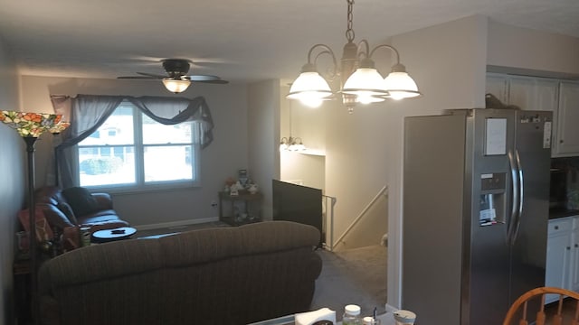 carpeted living room with ceiling fan with notable chandelier and baseboards