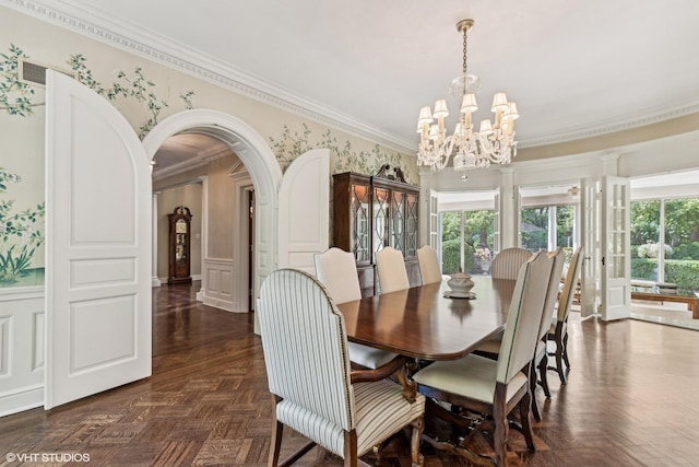 dining space with a wainscoted wall, arched walkways, crown molding, a notable chandelier, and a decorative wall