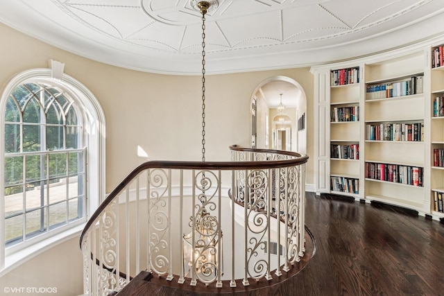 hallway featuring an upstairs landing, dark wood-type flooring, arched walkways, crown molding, and built in features