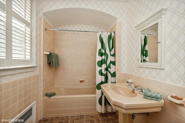 bathroom featuring shower / bath combo, radiator heating unit, wallpapered walls, tile walls, and a wainscoted wall