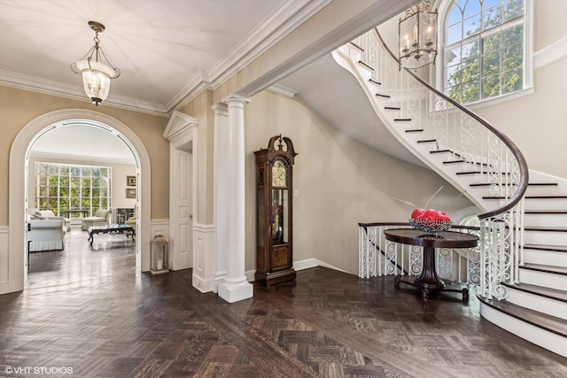 foyer featuring an inviting chandelier, ornamental molding, a wainscoted wall, and stairs
