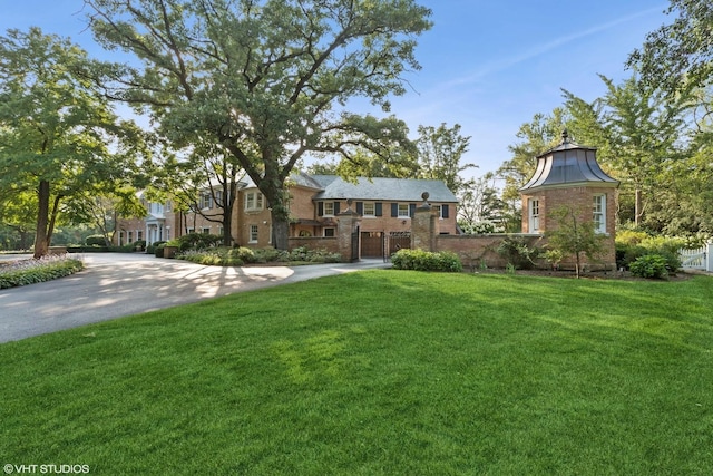 tudor-style house with driveway, brick siding, a front yard, and a garage