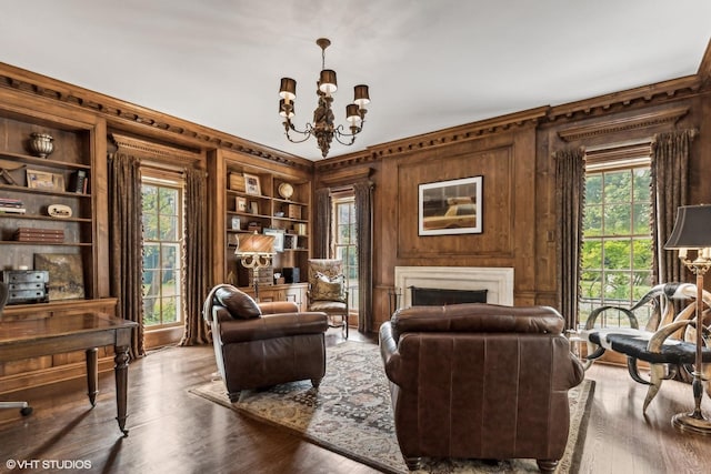 sitting room featuring wood finished floors, a chandelier, built in features, a fireplace, and wood walls