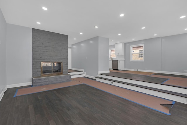unfurnished living room featuring recessed lighting, wood finished floors, a sink, baseboards, and a fireplace