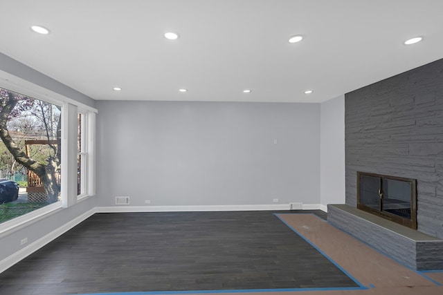 unfurnished living room featuring recessed lighting, dark wood finished floors, a stone fireplace, visible vents, and baseboards