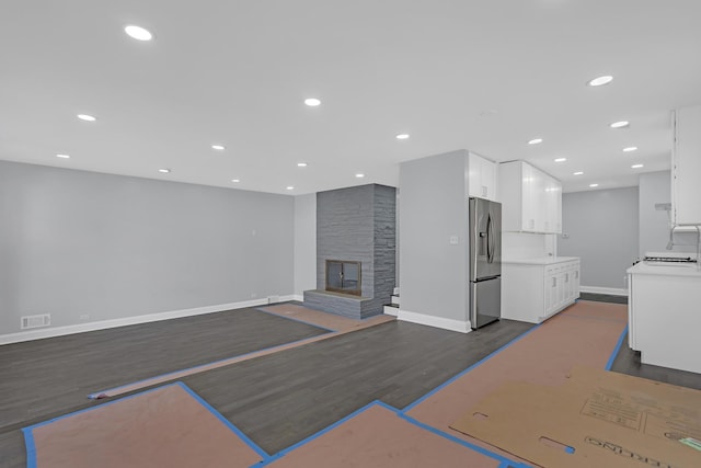 unfurnished living room featuring recessed lighting, dark wood finished floors, a stone fireplace, and baseboards