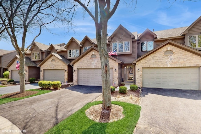 view of property featuring brick siding, a garage, and aphalt driveway