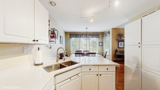 kitchen with an inviting chandelier, a peninsula, light countertops, white cabinets, and a sink
