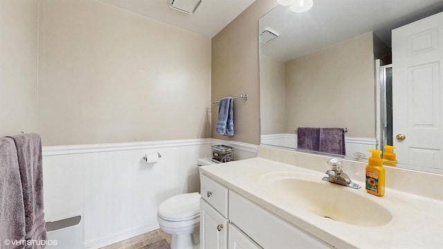 full bath with vanity, wainscoting, a shower with shower door, and toilet