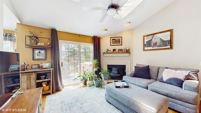 living room with a tiled fireplace, ceiling fan, wood finished floors, and vaulted ceiling