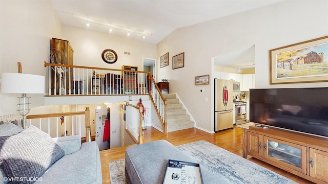 living room with light wood-type flooring, rail lighting, stairs, and lofted ceiling