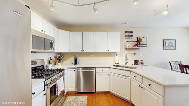kitchen featuring a peninsula, light wood-style floors, light countertops, a sink, and stainless steel appliances