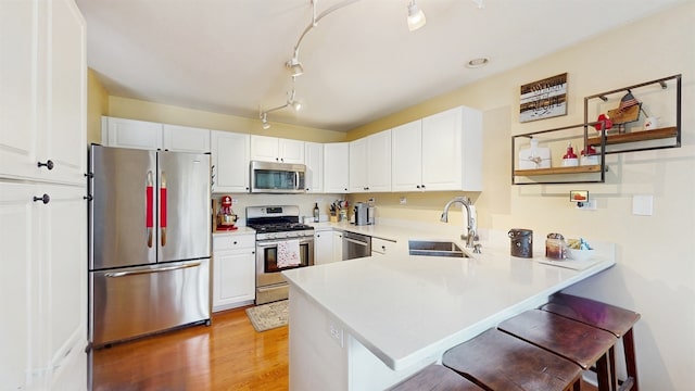 kitchen featuring a kitchen bar, appliances with stainless steel finishes, a sink, a peninsula, and white cabinetry