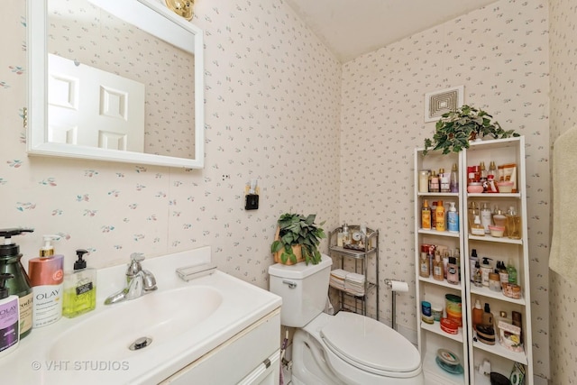 bathroom featuring vanity, visible vents, wallpapered walls, and toilet