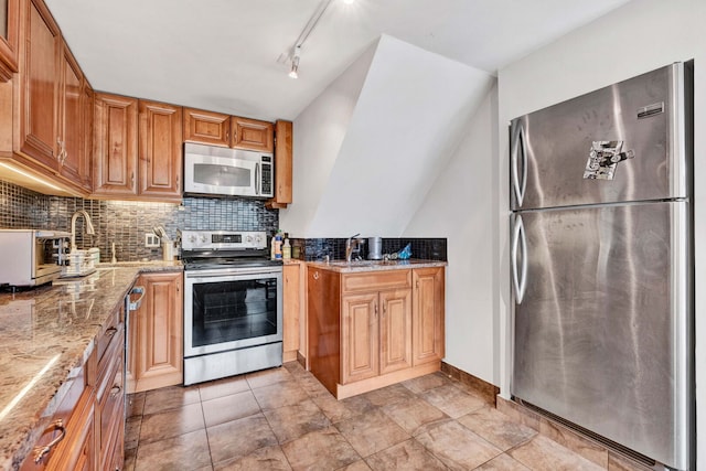 kitchen with light stone countertops, appliances with stainless steel finishes, backsplash, a sink, and baseboards