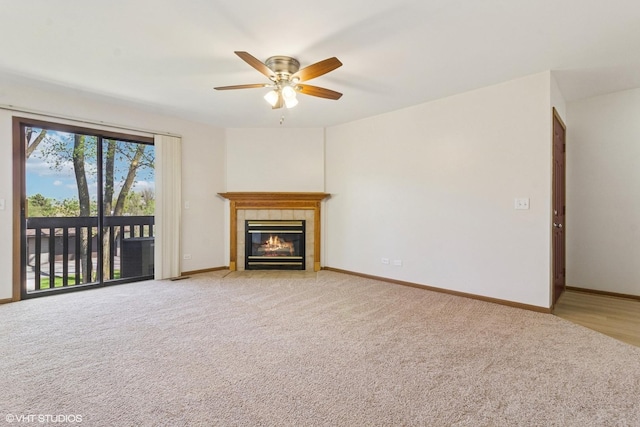 unfurnished living room with baseboards, ceiling fan, a fireplace, and light carpet
