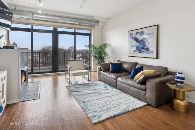 living area featuring a wall of windows, baseboards, rail lighting, and wood finished floors
