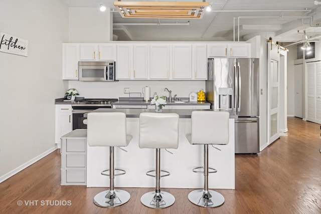 kitchen featuring dark countertops, appliances with stainless steel finishes, a breakfast bar, white cabinetry, and dark wood-type flooring