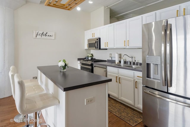 kitchen with a kitchen breakfast bar, appliances with stainless steel finishes, dark countertops, dark wood finished floors, and a sink