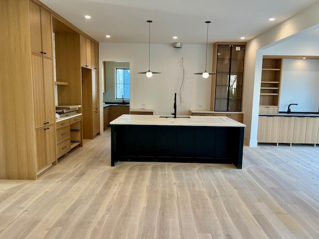 kitchen featuring light countertops, modern cabinets, a sink, a spacious island, and light wood-style flooring