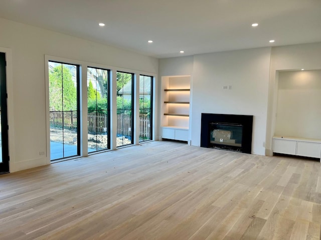 unfurnished living room with light wood-style flooring, a glass covered fireplace, recessed lighting, and built in features