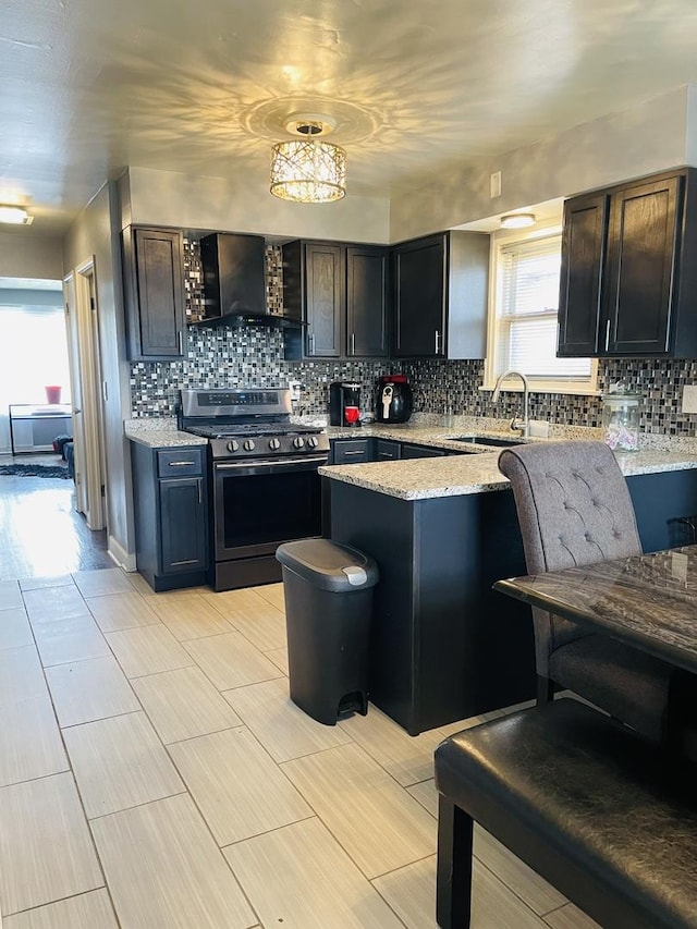 kitchen with a sink, stainless steel gas range oven, wall chimney range hood, and decorative backsplash