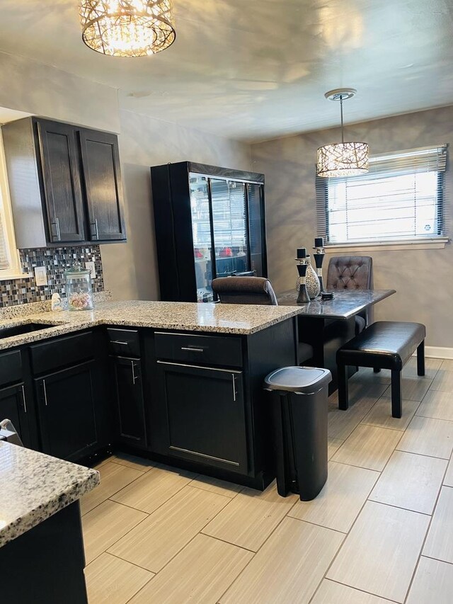 kitchen with tasteful backsplash, dark cabinets, wood tiled floor, an inviting chandelier, and a peninsula